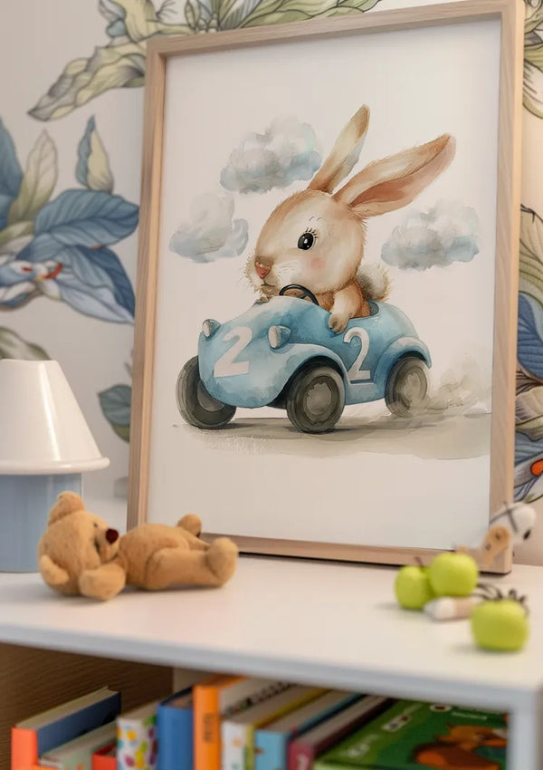 Op een kinderkamerplank staat een ingelijst CollageDepot Konijn In Blauwe Raceauto Schilderij van een konijn dat in een blauwe raceauto rijdt met het nummer twee erop. Op de plank staat ook een kleine tafellamp, een speelgoedteddybeer, groene appels en verschillende kinderboeken. De achtergrond is voorzien van bloemenbehang.,Lichtbruin