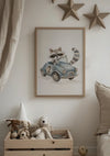 Aan de muur hangt een ingelijste foto van een wasbeer die een vintage blauw auto-kunstwerk bestuurt met het nummer 2 erop. Hieronder staat een houten kist met knuffels, waaronder een wit konijn, een beige beer en een bruine beer. Aan de muur zijn drie houten sterdecoraties gemonteerd. Het kunstwerk heet "Wasbeer in Blauwe Vintage Auto Schilderij" van CollageDepot.,Lichtbruin