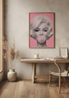 Het minimalistische interieur is voorzien van een houten bureau met een stoel, kleine potplanten en boeken. Boven het bureau hangt een ingelijst Bubblegum Beauty Popart Schilderij van CollageDepot van een vrouw met blond haar die kauwgom blaast tegen een roze achtergrond. De kamer heeft aardetinten en lichte houten vloeren.