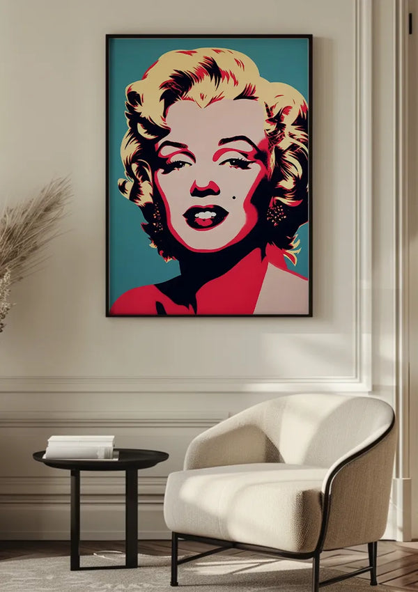 Aan een beige muur hangt een ingelijst pop-art portret van een vrouw met blond haar en rode lippen, dat doet denken aan een schilderij van Marilyn Monroe, boven een fauteuil en een rond zwart bijzettafeltje. De CollageDepot Marilyn Monroe In Popart Schilderij wanddecoratie heeft gedurfde kleuren, waaronder geel, rood en blauw. Links staat een vaas met gedroogde planten.